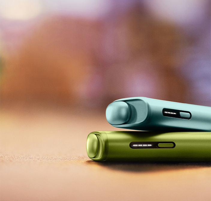 Dispositivo IQOS ILUMA i ONE Azul Claro sobre dispositivo IQOS ILUMA i ONE Verde, em fundo desfocado